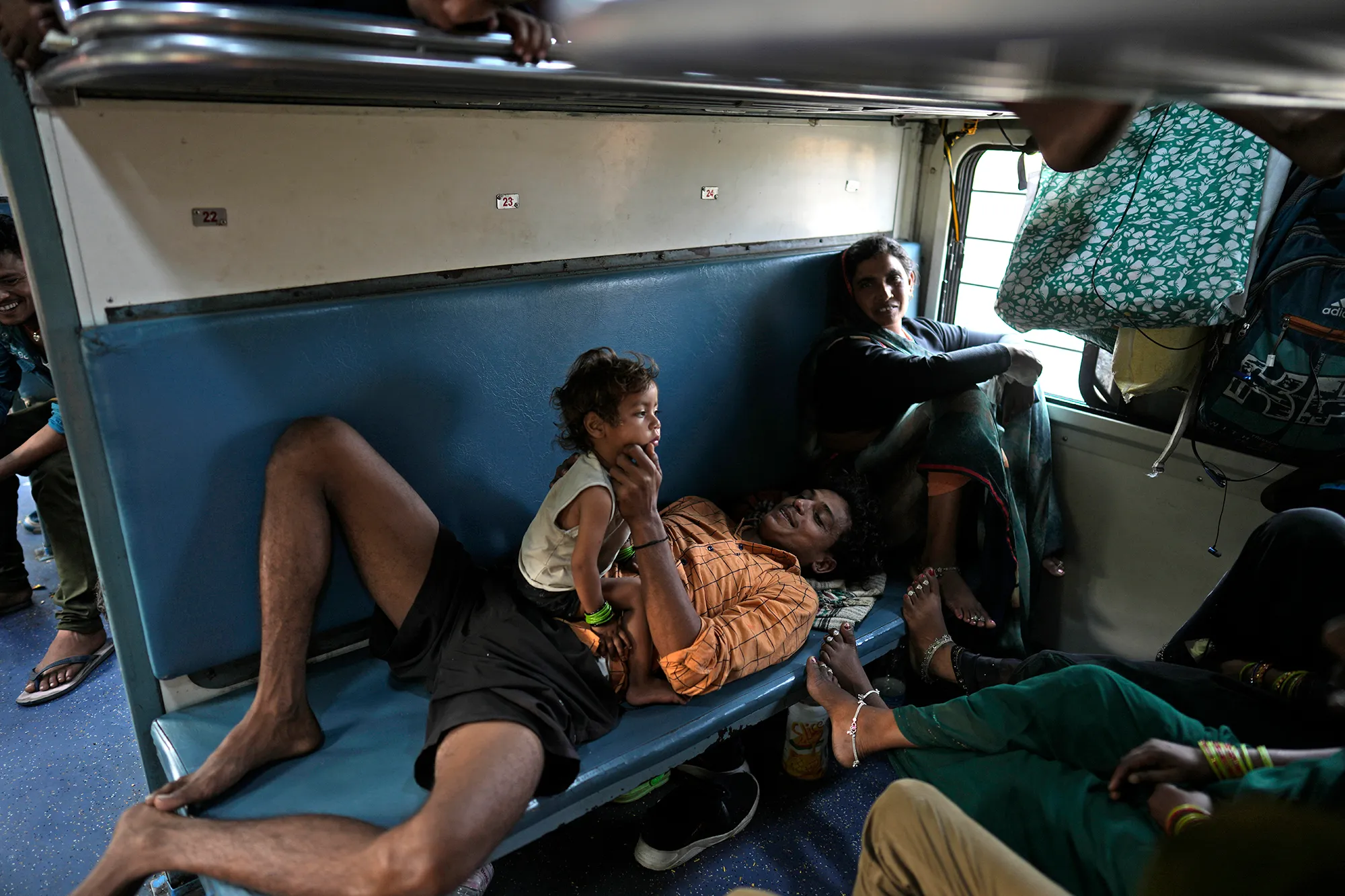A man laying down on a bench holding a child on an Indian train