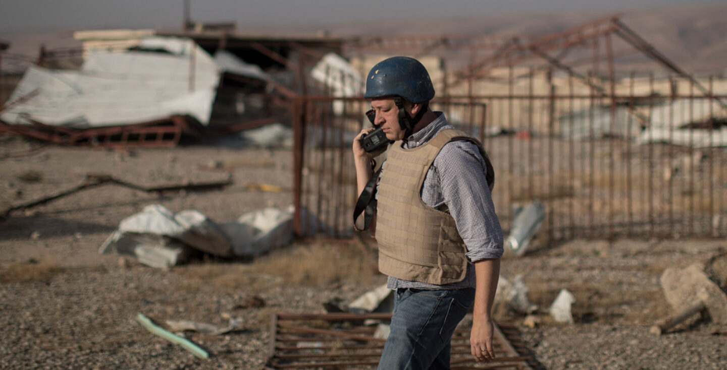A photographer carrying a camera wearing a helmet and flak jacket