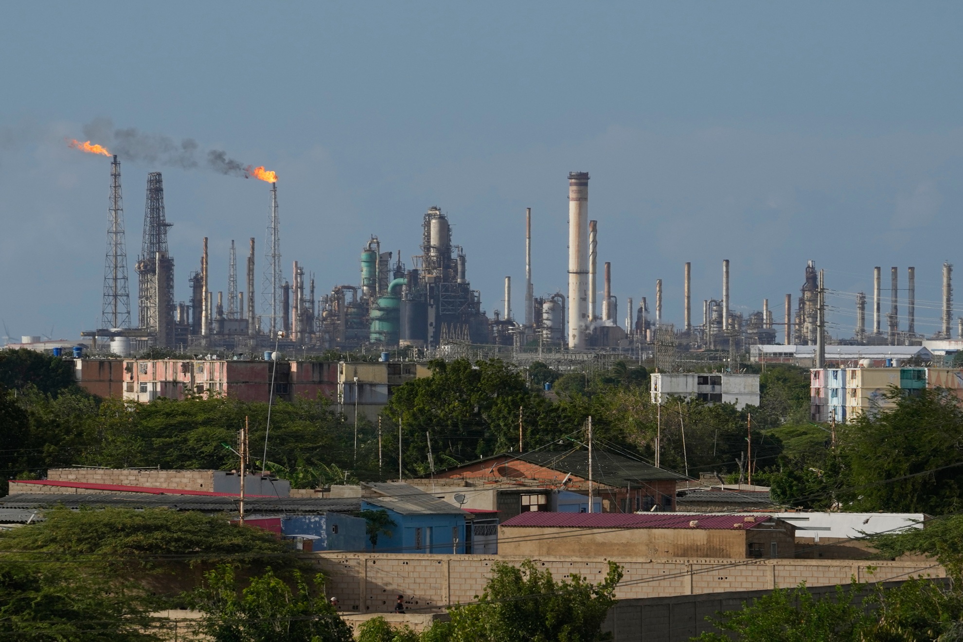 Photo of flames rising from the Amuay refinery in Los Taques, Venezuela, with the neighborhood in the front of the photo and the oil refinery in the background